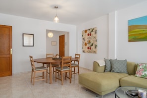 A dining area with a wooden table and chairs, a sofa, and a painting on the wall.