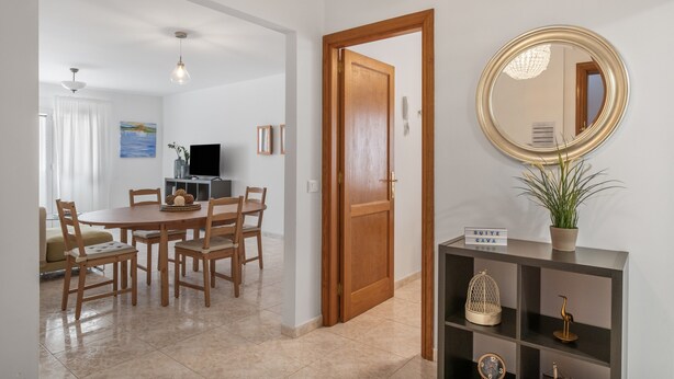 Een eethoek met een ronde tafel en stoelen, een houten deur, een spiegel en een plank met decoratieve spullen.
