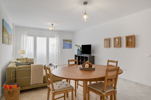 A living room with a round wooden dining table, a sofa, a TV, and a window with curtains.