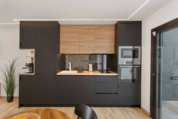 Una cocina moderna con armarios oscuros, encimera de madera y electrodomésticos integrados, incluyendo un microondas y un horno.