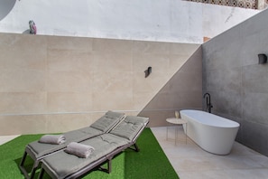 Un baño moderno con una bañera independiente, dos tumbonas con toallas y una pequeña mesa con un vaso.