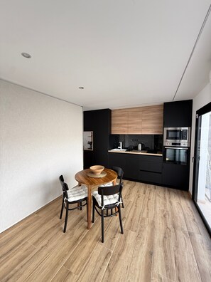 Une cuisine moderne avec des meubles de rangement noirs, une table à manger en bois et deux chaises.