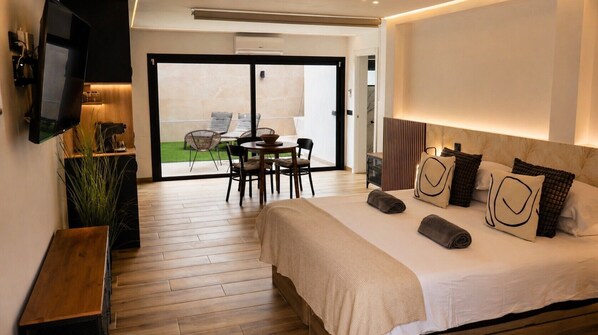 Ein modernes Hotelzimmer mit einem großen Bett, einem Fernseher, einem Essbereich mit Stühlen und Blick ins Freie.