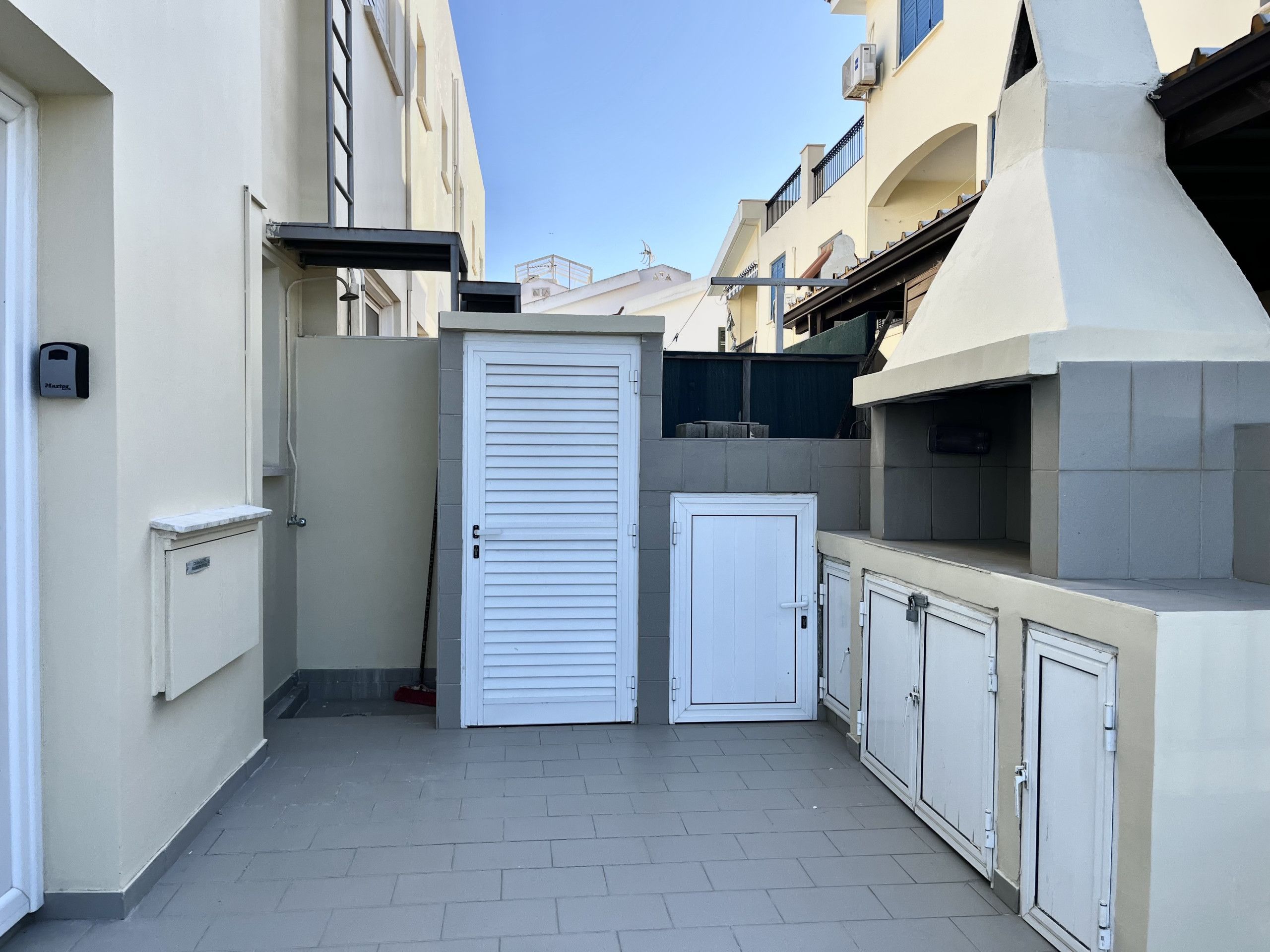 A narrow urban alleyway with a closed white door, a small cabinet, and a tiled floor.