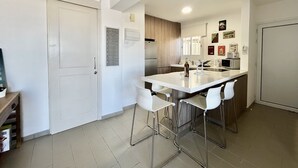Et moderne køkken med en central ø, hvide barstole, et køleskab og en mikrobølgeovn.