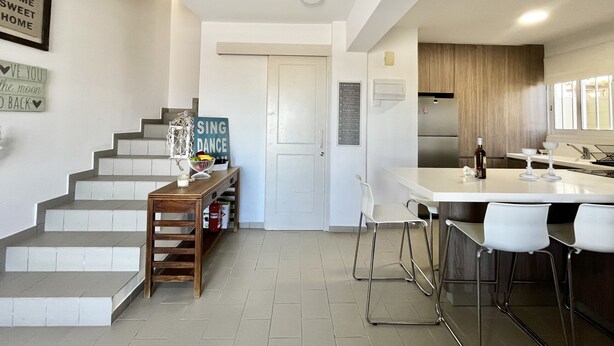 Et moderne køkken med en central ø, barstole og en trappe, der fører til en etage ovenpå.