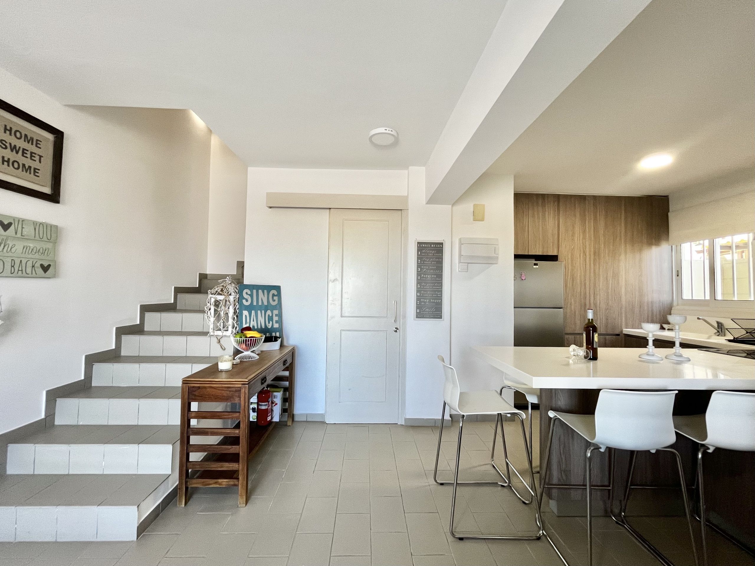 A modern kitchen with a central island, bar stools, and a staircase leading to a second floor.