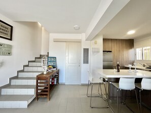 Una cocina moderna con una isla central, taburetes de bar y una escalera que lleva a un segundo piso.