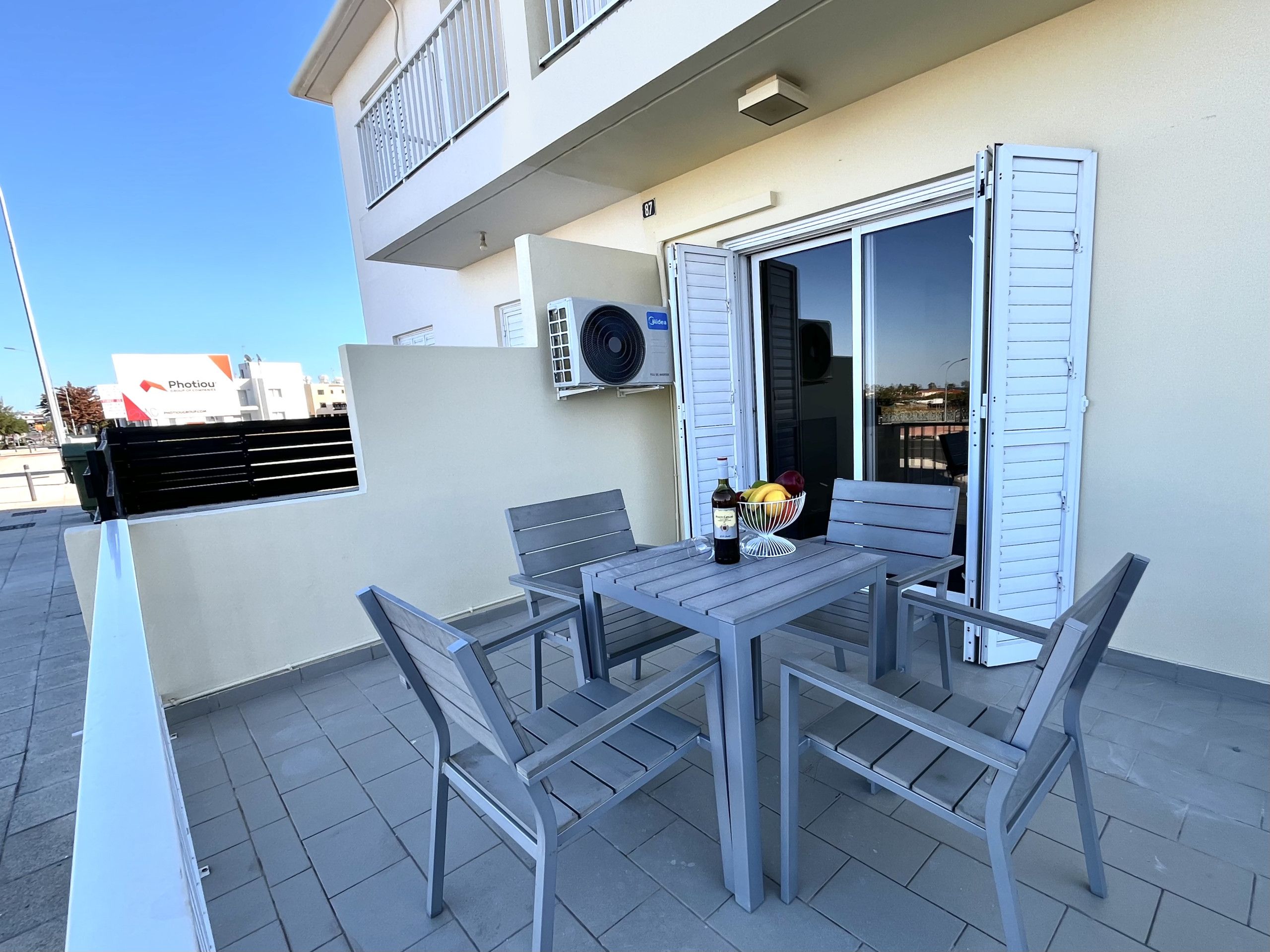 An outdoor patio with a table, chairs, and a bowl of fruit and a bottle of wine.