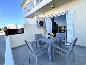 Un patio al aire libre con una mesa, sillas, un cuenco de fruta y una botella de vino.