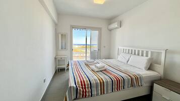 A bedroom with a bed, a bedside table, a nightstand, a mirror, and a sliding glass door leading to a balcony.
