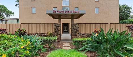 A building with a sign reading '73 North Kihei Road' and a pathway leading to the entrance.