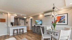 A modern living room with a dining area, a kitchen with a bar, and a TV mounted on the wall.