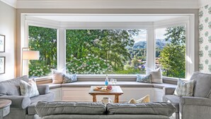 A bay window seating area with a view of a lush garden and mountains.
