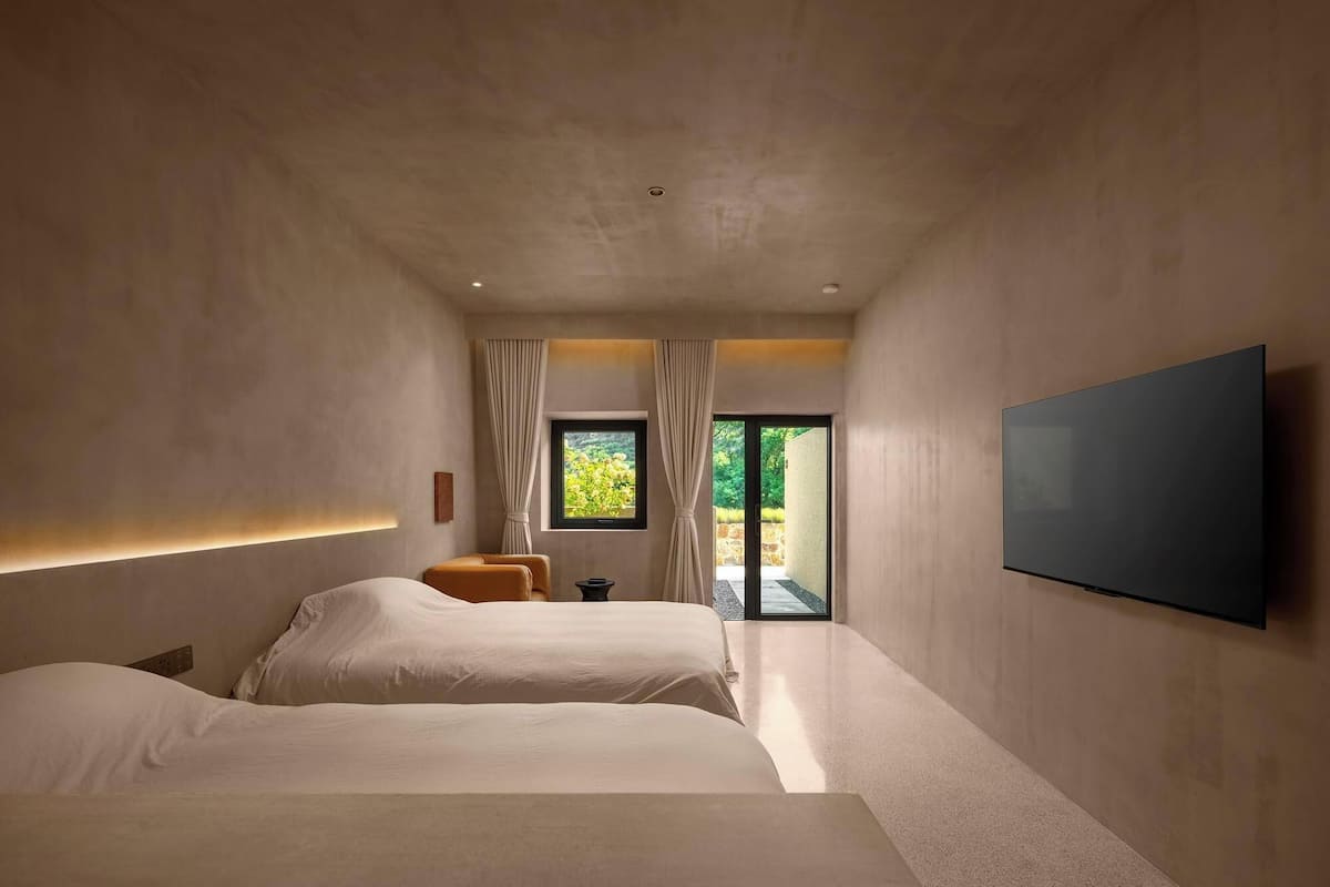 Une chambre moderne avec deux lits, une télévision et une vue sur la verdure par la fenêtre.
