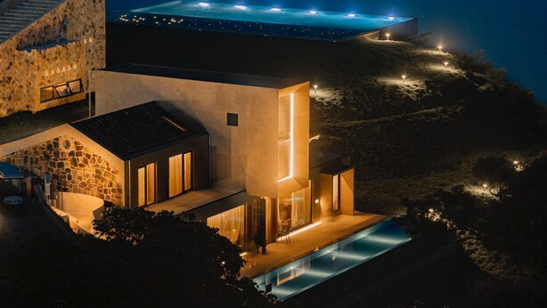A modern coastal property with a swimming pool, stone architecture, and a view of the sea.