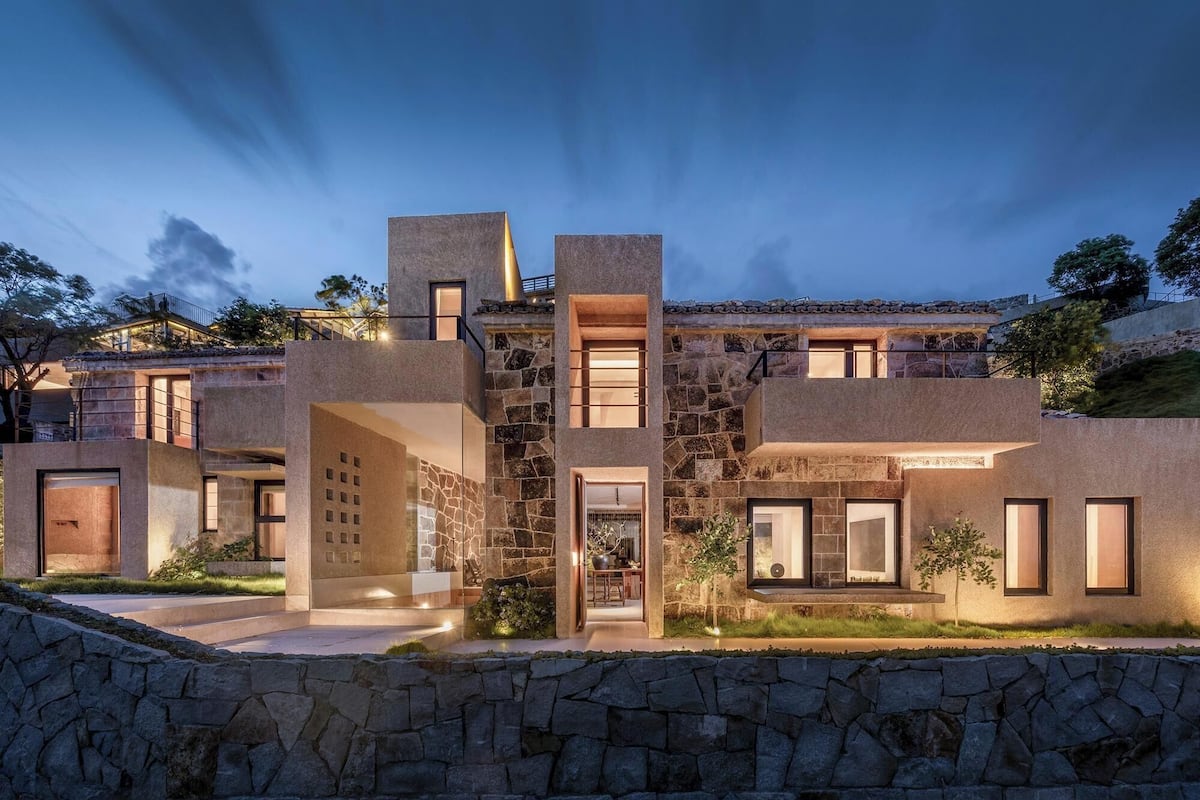 Une maison moderne avec une façade en pierre, plusieurs entrées et un intérieur bien éclairé, visible à travers les fenêtres.