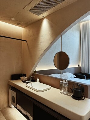 Een moderne hotelbadkamer met een gebogen wastafel, een grote spiegel, een wastafel en een koffieapparaat.