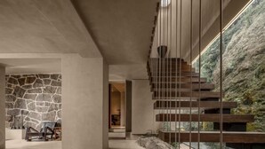 A modern interior with a stone wall, a staircase with wooden steps, and a view of a rocky landscape.