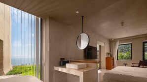 Una habitación de hotel moderna con un balcón amplio, una bañera, un tocador con espejo, una cama y un televisor.