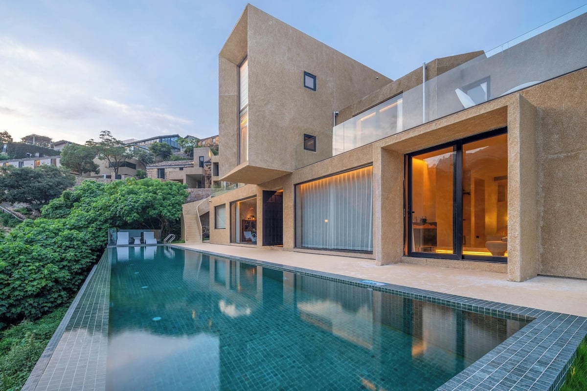 Une maison moderne dotée d’une piscine, de grandes fenêtres et offrant une vue sur les environs.