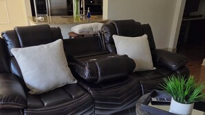 Ein modernes Wohnzimmer mit einer schwarzen Ledersofa, einem kleinen runden Tisch mit einer Pflanze und einer Küche im Hintergrund.