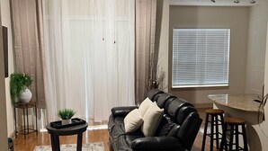 Ein Wohnzimmer mit einem schwarzen Ledersofa, einem kleinen runden Tisch, einem Deckenventilator und einem Fenster mit Jalousien.