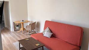 A living room with a red sofa, a wooden coffee table, a small round table with a chair, and a framed picture on the wall. - Charming 1-bedroom apartment close to downtown Seattle! (Seattle)