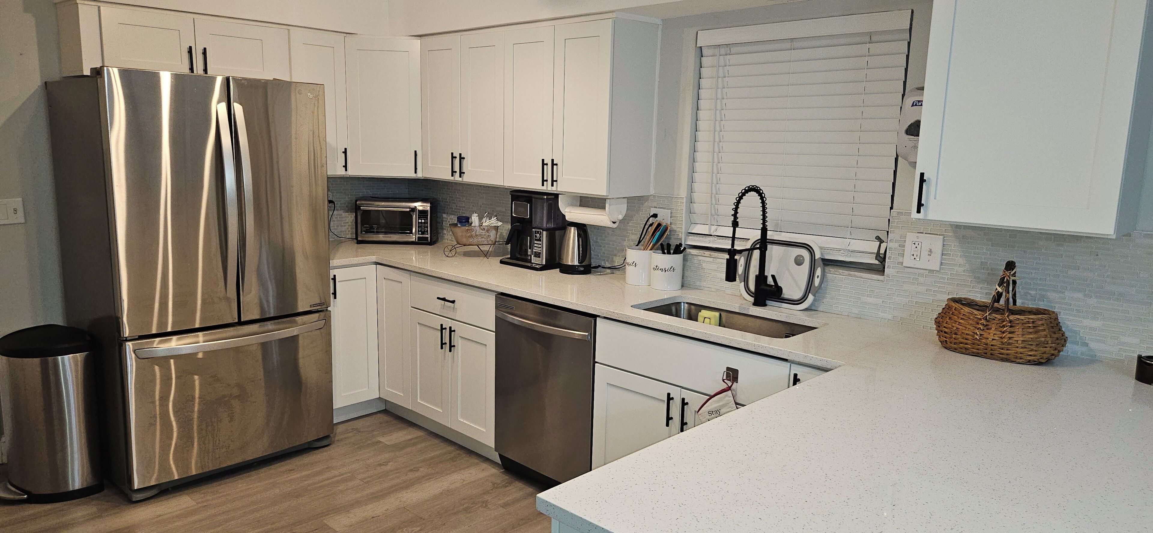 A modern kitchen with stainless steel appliances, white cabinetry, a built-in dishwasher, and a coffee maker.