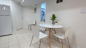 Une petite cuisine moderne, dotée d’appareils électroménagers blancs et d’un coin repas avec une table ronde et quatre chaises.