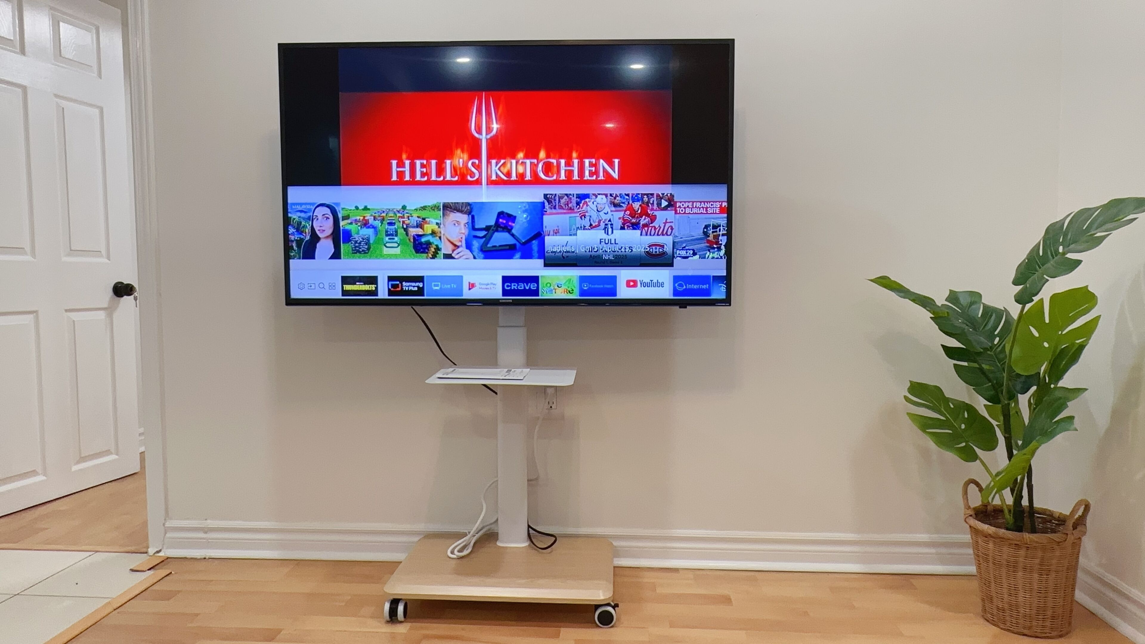 A flat-screen TV mounted on a white stand with a wooden platform, displaying a cooking show.