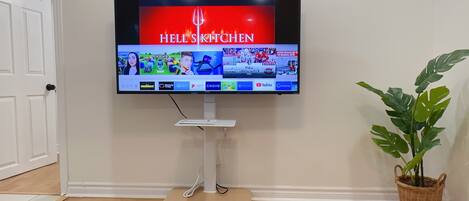 A flat-screen TV mounted on a white stand with a wooden platform, displaying a cooking show.