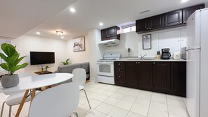 Une cuisine moderne avec des meubles de couleur sombre, une cuisinière blanche et un coin repas comprenant une table et des chaises blanches.