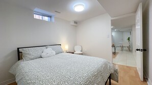Une chambre à coucher comprenant un lit, une table de chevet, une commode, une fenêtre et une porte donnant sur une salle de bain.