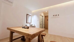 A modern hotel room with a wooden dining table, a mirror, and a small kitchenette.
