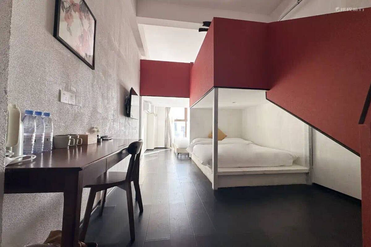 Camera d'albergo compatta con un letto a castello, una scrivania con sedia, un tavolino e una bottiglia d'acqua.