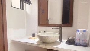 A bathroom with a white sink, a large mirror, and a shelf with bottled water and a cup.