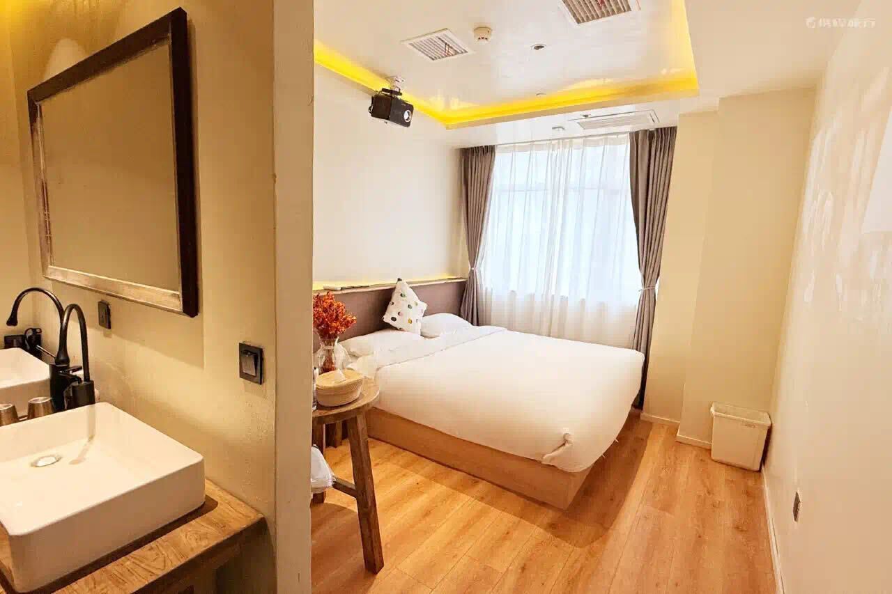 Ein Hotelzimmer mit einem großen Bett, einem Nachttisch mit einer Vase, einem Spiegel und einem Fenster mit Vorhängen.