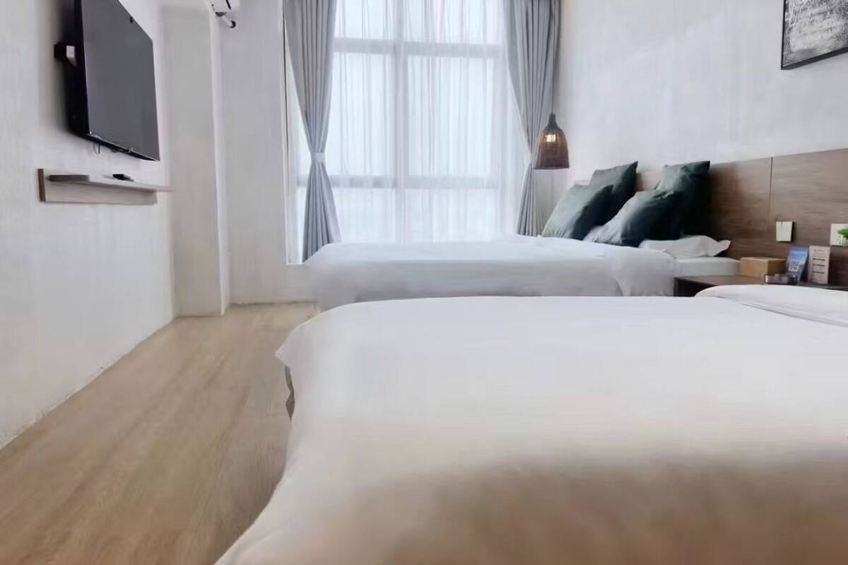Camera d'albergo con due letti, una televisione, una finestra con tende e un comodino con una lampada.