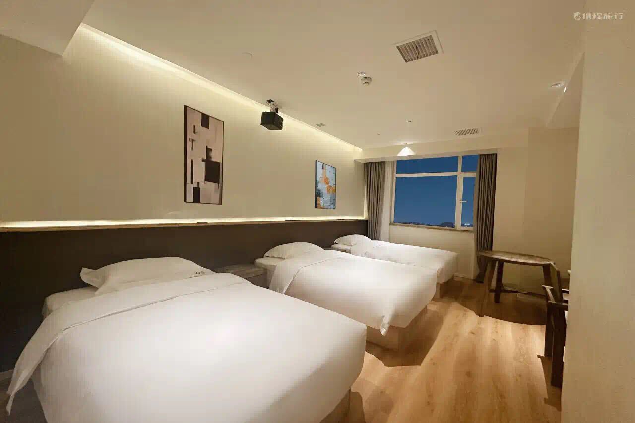 Habitación de hotel con tres camas, una mesita y una ventana con cortinas.