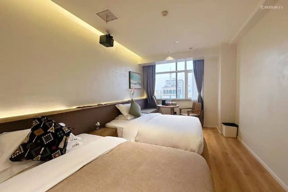 Camera d'albergo con due letti, un tavolino, una sedia e una finestra vista città.
