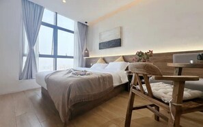 A modern hotel room with a large bed, a wooden nightstand, a small table, and a view of the city through large windows. - Chenshe Hotel Xiaonanmen Morning Market (Xi'an)
