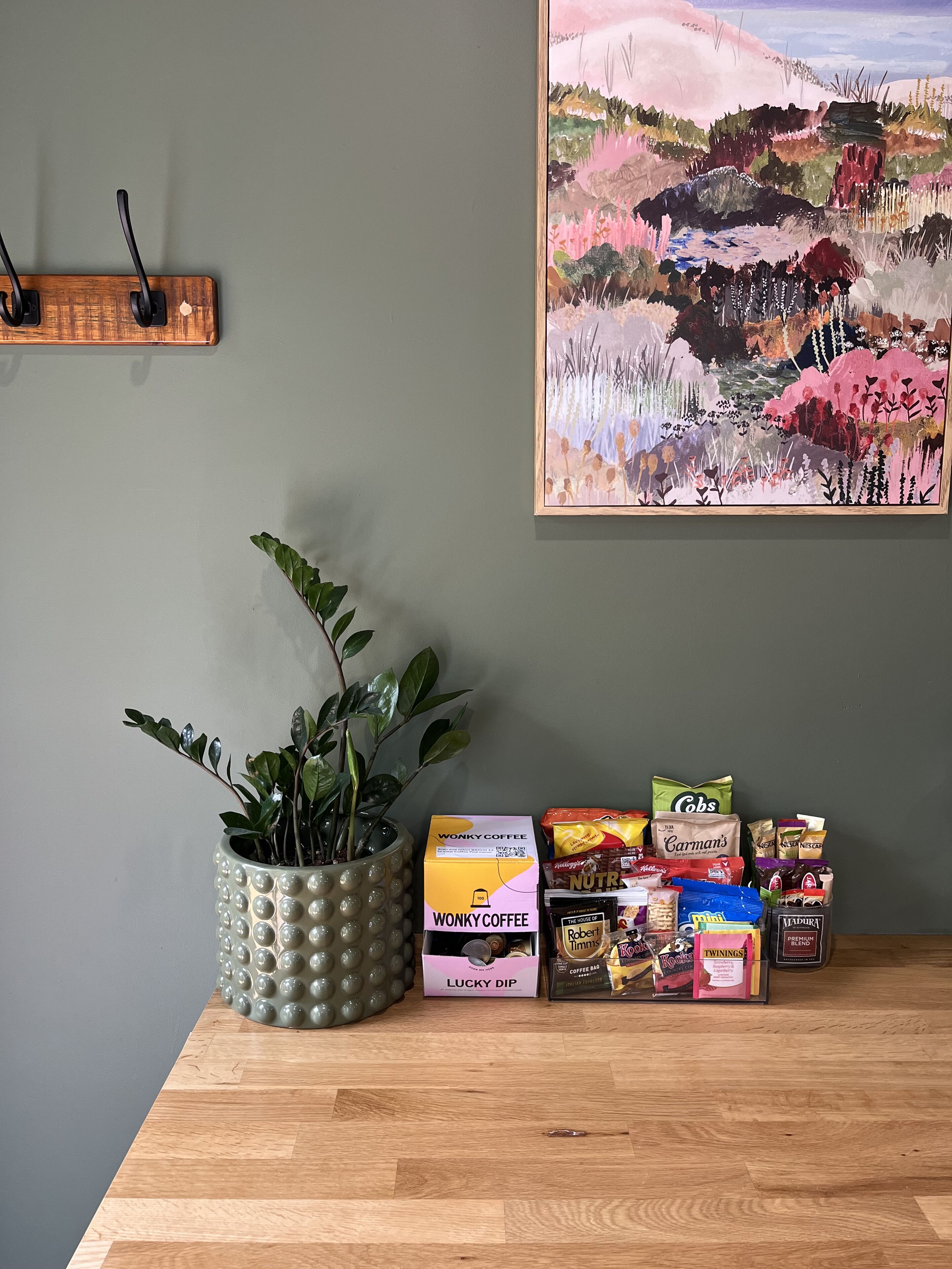 Una mesa de madera con una planta en maceta, una cafetera y diferentes bolsitas de café y té.