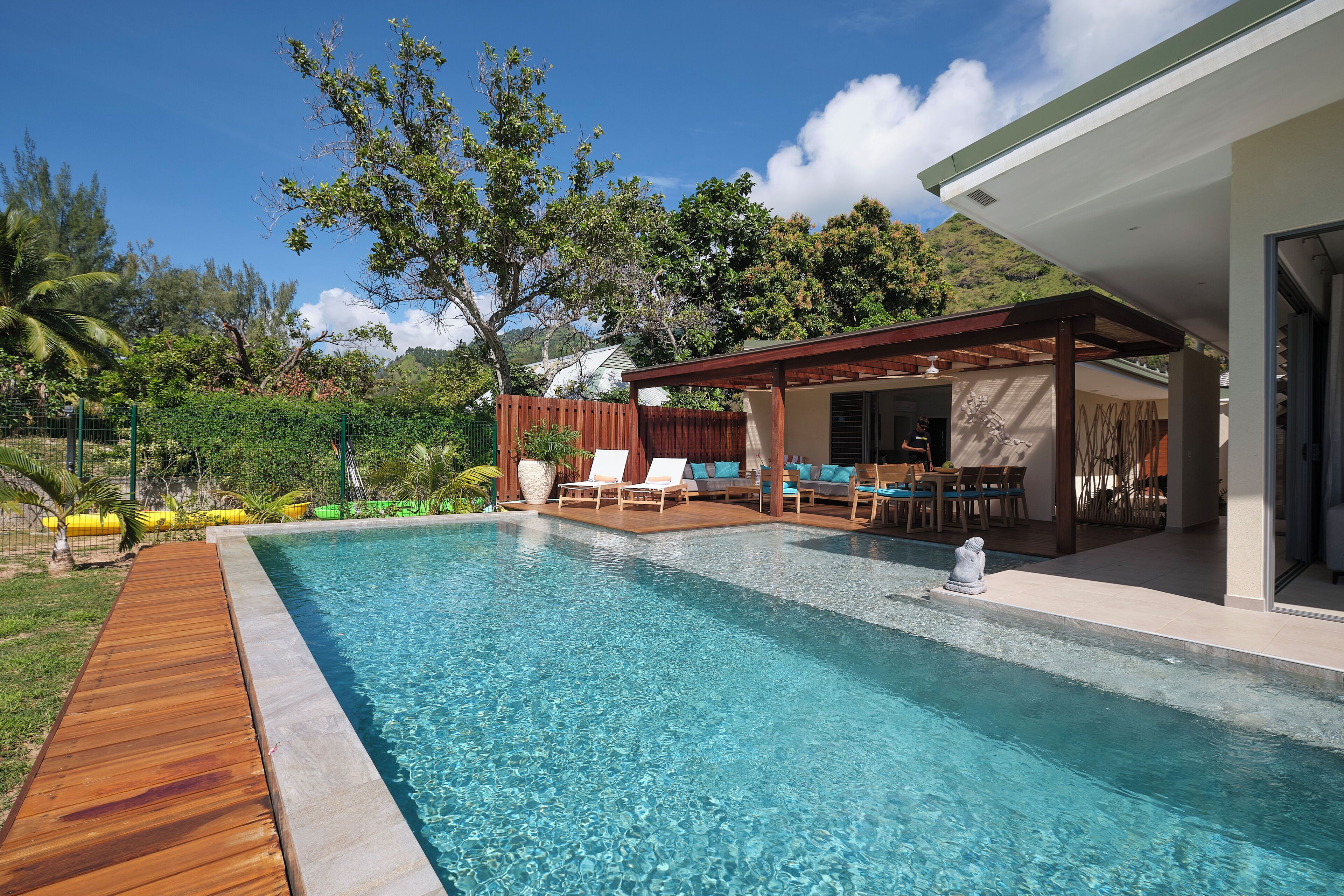 A swimming pool with a wooden deck, lounge chairs, and a covered patio area.