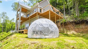 A two-story house with a large deck and a geodesic dome structure in the yard.