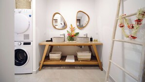 Une petite salle de bain équipée d’un lave-linge, de deux éviers, d’un miroir et d’une plante décorative.