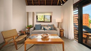Un salon avec un canapé, une table basse en bois, un fauteuil en osier, un ordinateur portable et une fenêtre avec des stores.