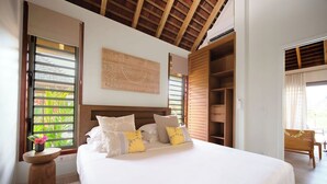 Une chambre avec un grand lit, une tête de lit en bois et une vue sur la verdure par la fenêtre.