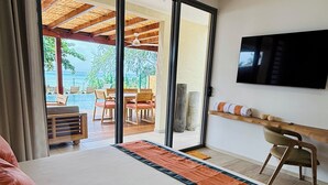 Habitación de hotel con cama, televisión montada en la pared, escritorio y vista al área de piscina exterior.