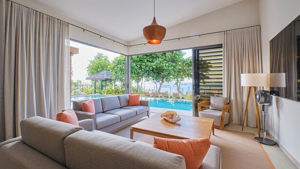 Una sala moderna con sofá, mesa de centro y vistas a una piscina y vegetación.